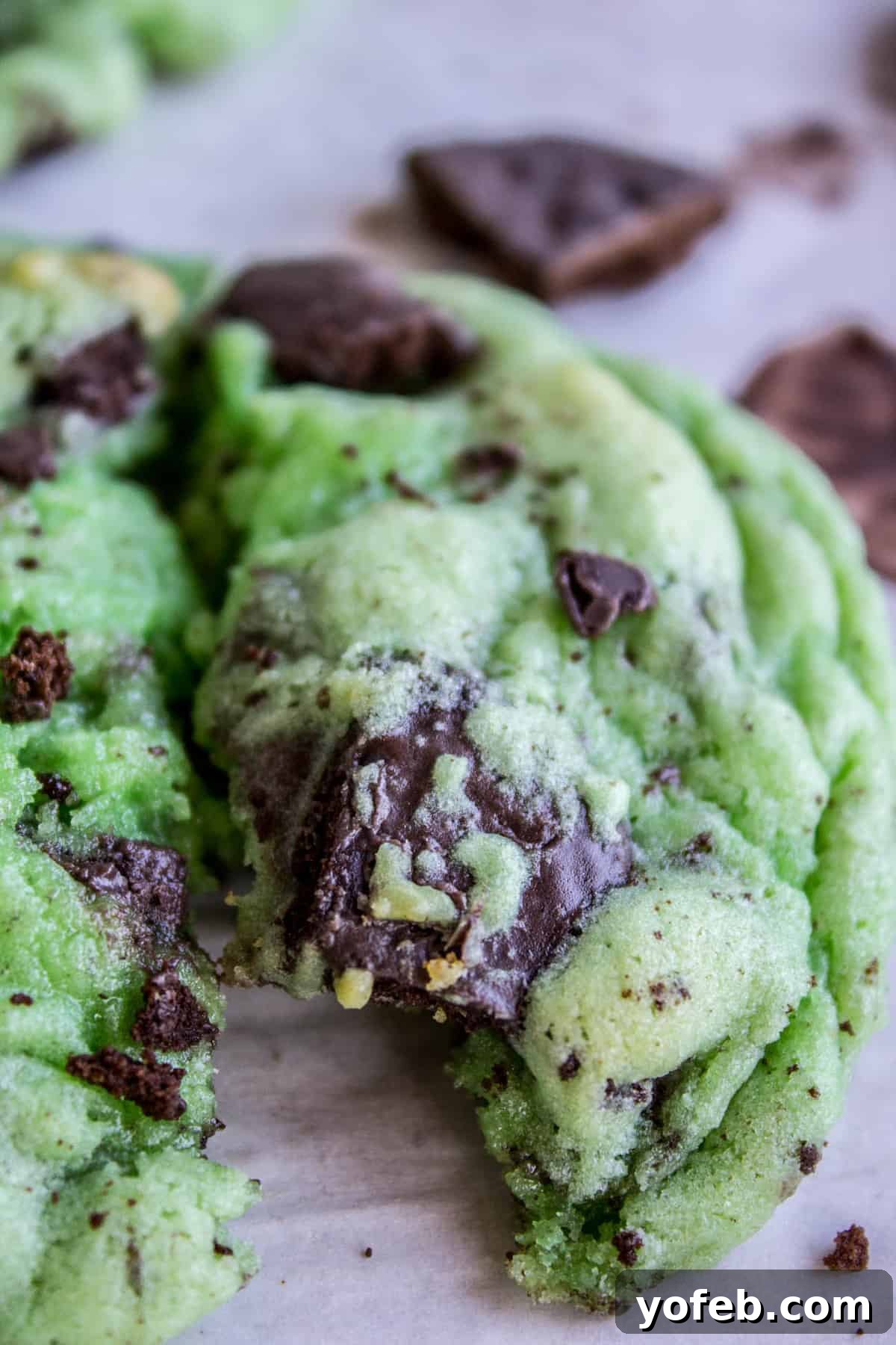 Thin Mint Mint Cookies: A double mint cookie dream with Girl Scout Thin Mints inside, perfect for St. Patrick's Day or any mint chocolate craving. #cookies #stpatricksday #thinmint #girlscout #green #mint A vibrant green Thin Mint Mint Cookie broken in half, revealing the soft, chewy interior and embedded chunks of Girl Scout Thin Mints.