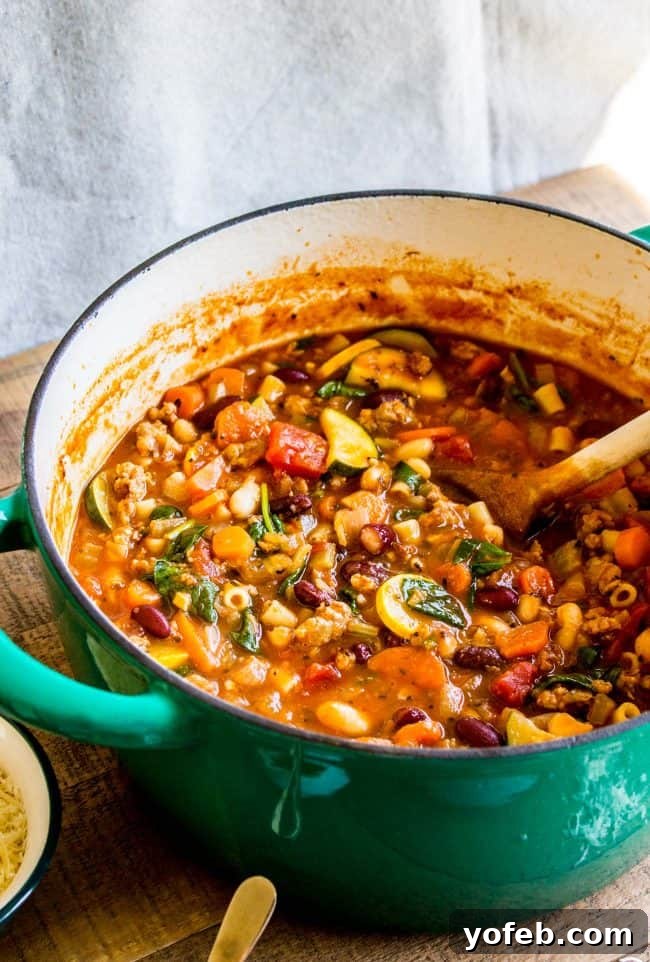 Hearty Minestrone with Sausage Simmering in a Pot minestrone soup with sausage in a pot with a wooden spoon.