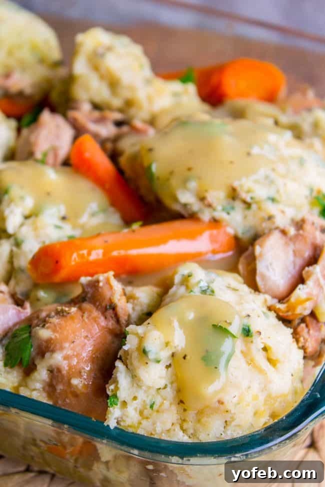 Hearty Chicken and Dumplings with Savory Gravy A serving of Crockpot Chicken and Dumplings in a glass dish, showing the texture of the chicken, carrots, and the thick gravy.