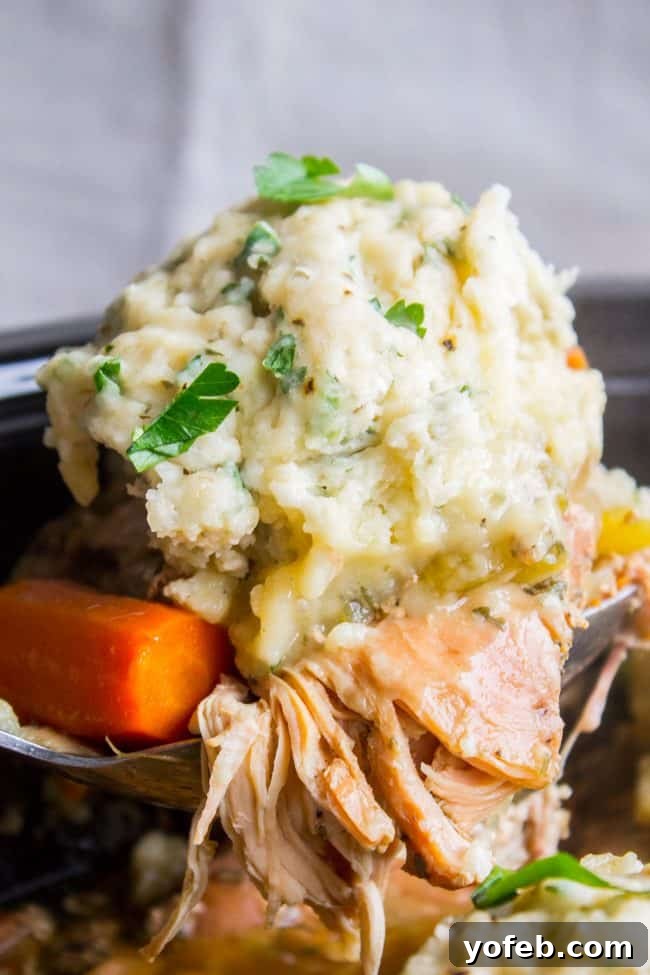 Scooping out Crockpot Chicken and Dumplings A metal spoon lifting a hearty portion of shredded chicken, cooked carrots, and a homemade dumpling from the crockpot.