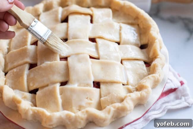 Grandma's Secret Apple Pie 15 A hand brushing a mixture of milk and egg over a lattice pie crust before baking, creating a beautiful golden sheen.