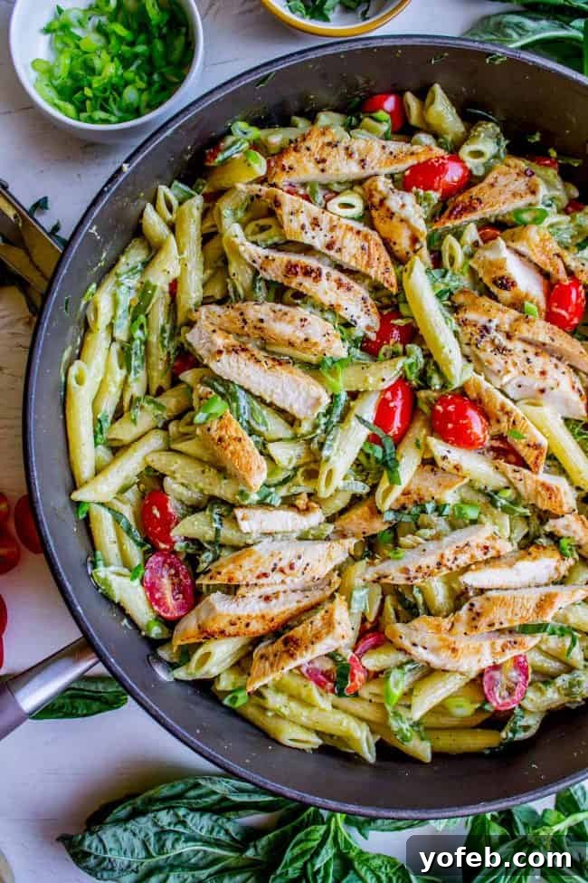 Delicious 30-Minute Pesto Penne with Chicken and Cherry Tomatoes A skillet filled with creamy chicken penne pesto pasta, adorned with bright red cherry tomatoes and green basil leaves, ready to be served for a quick and easy dinner.