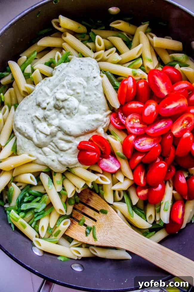 Pesto Penne with Fresh Basil and Tomatoes A beautifully arranged bowl of penne pasta with creamy pesto sauce, fresh basil, and ripe cherry tomatoes, accompanied by a wooden spoon.