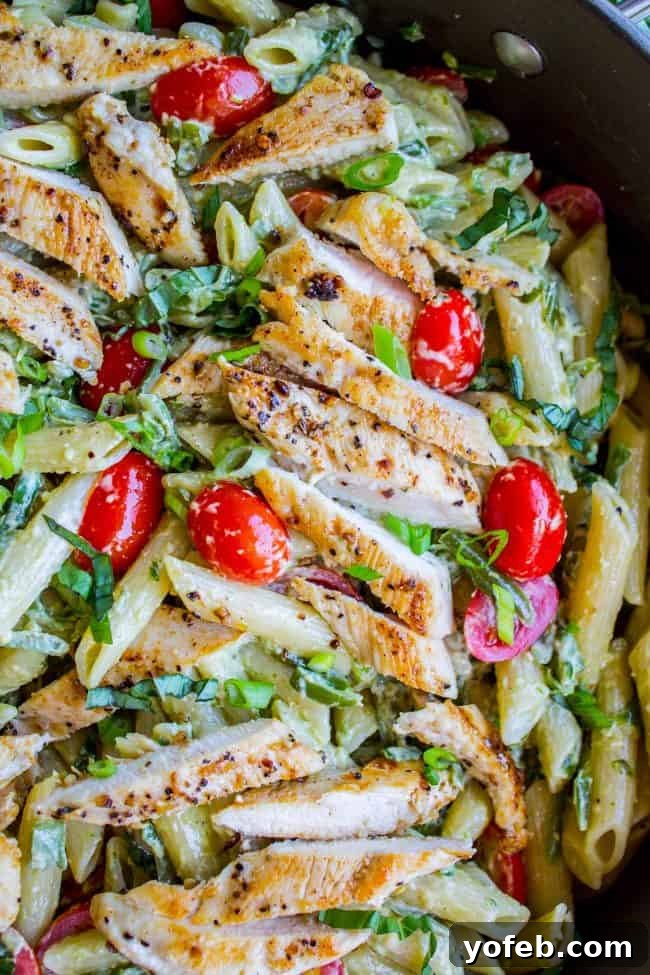 Creamy Pesto Penne with Basil and Tomatoes A vibrant bowl of creamy pesto penne pasta, garnished with fresh basil leaves and halved cherry tomatoes, inviting a delicious tasting experience.
