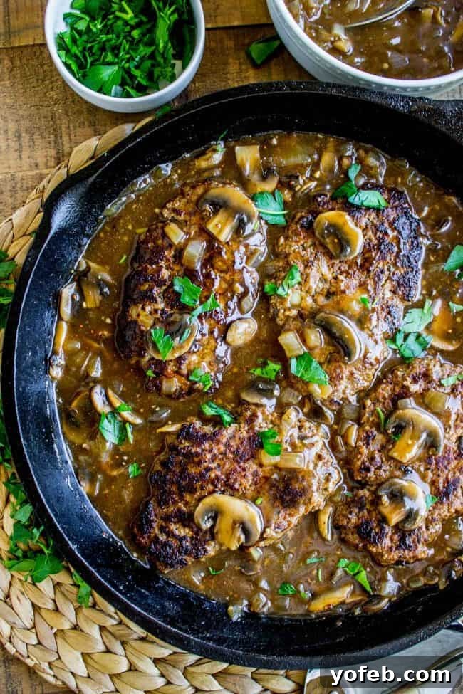 Homemade Salisbury Steak Recipe with Mushroom Gravy - Quick & Easy Dinner Idea. A one-skillet marvel featuring seasoned ground beef patties and a rich, savory mushroom gravy. Perfect for family meals. #SalisburySteak #MushroomGravy #SkilletDinner #GroundBeef #ComfortFood A rustic cast iron skillet filled with golden-brown Salisbury steaks, generously coated in a rich, dark mushroom gravy, ready to be served. The comforting aroma practically wafts from the image.