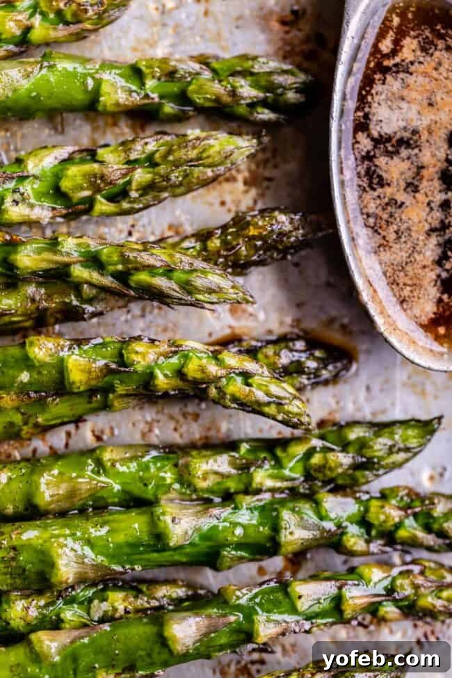 The effortless process of creating perfect roasted asparagus with a gourmet browned butter sauce. Simple, yet profoundly delicious. #HomeCooking #RecipeIdeas #Foodie A side view of a baking sheet featuring roasted asparagus, with a small bowl of savory browned butter nearby.