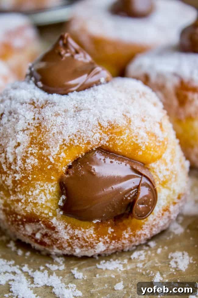 A close-up of a Nutella donut filled with creamy chocolate hazelnut spread, with generous dollops on top and even more oozing from the side.