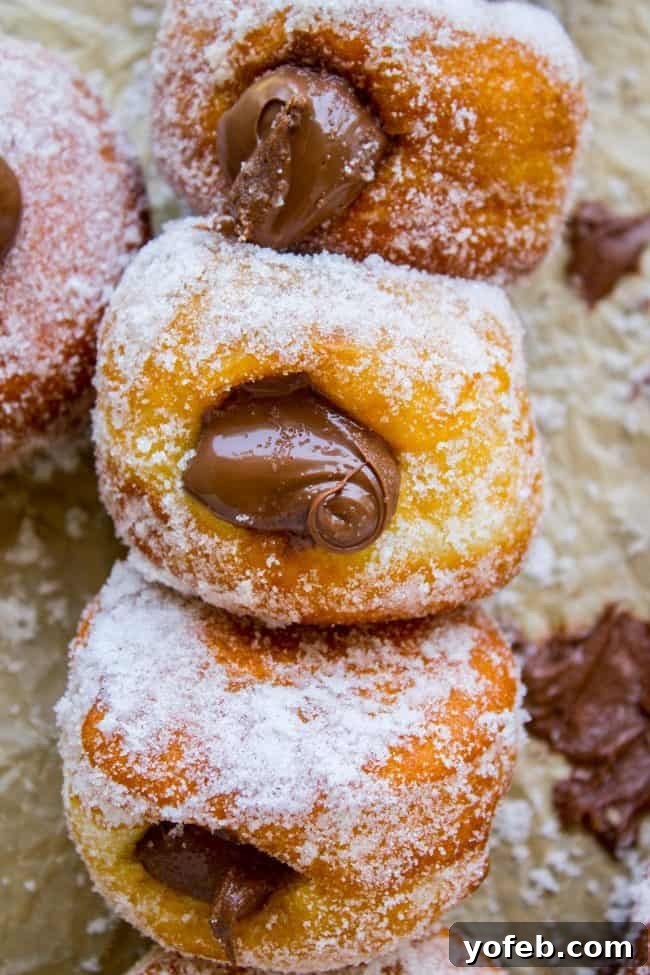 Experience ultimate indulgence with these Nutella-filled donuts, featuring a generous, warm chocolate hazelnut center that perfectly complements the fluffy yeast dough. A delectable stack of Nutella-filled donuts, with the rich chocolate hazelnut filling visible at the edges, inviting you to take a bite.