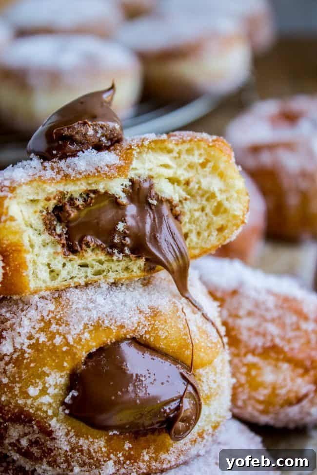 Indulge in a perfect bite of a Nutella stuffed donut, where fluffy dough meets rich, warm chocolate hazelnut spread, creating an unforgettable dessert experience. A Nutella-filled donut with a bite taken out, revealing the creamy, spreadable chocolate hazelnut filling and the soft, airy interior of the donut.