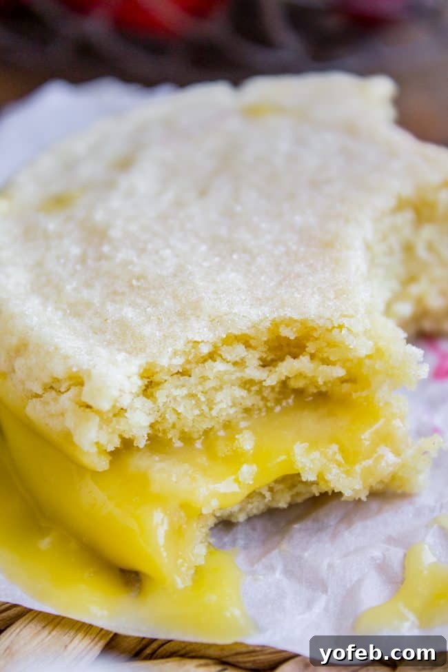 Refreshing Lemon Desserts - Lemon Curd Sugar Cookie Sandwiches A lemon curd sugar cookie sandwich shown from a side angle, revealing the thick, glossy layer of lemon curd between two cookies.