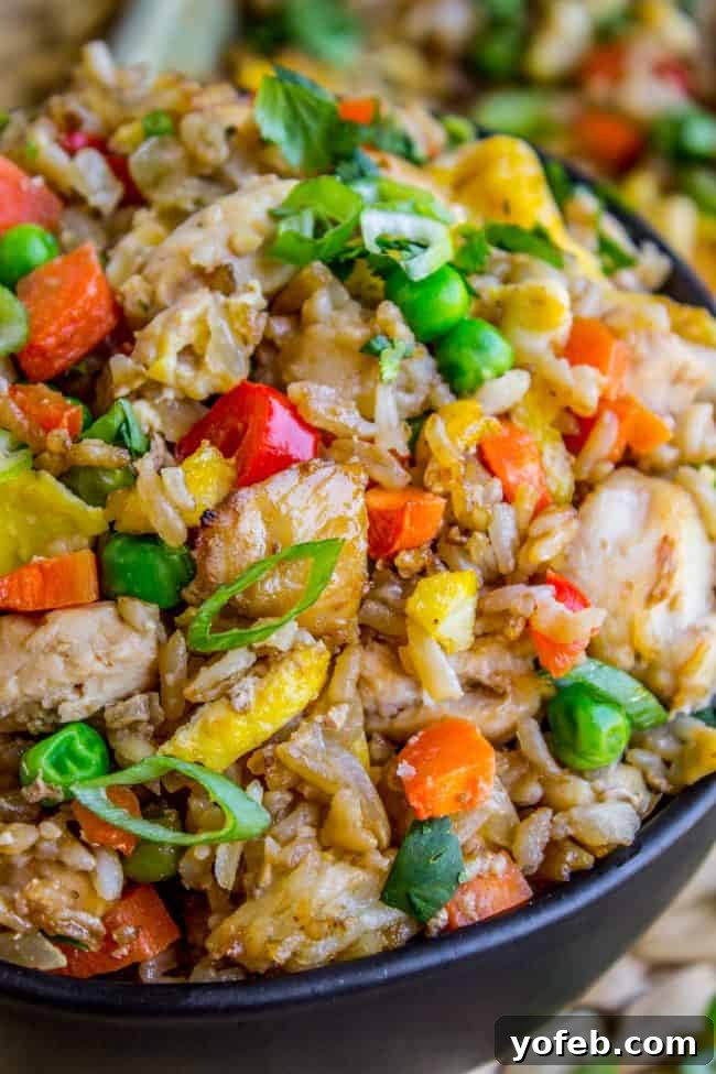 A bowl of chicken fried rice with colorful vegetables and fresh herbs