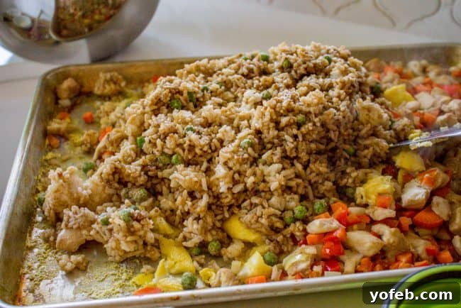 Day-old rice being spread evenly over par-cooked chicken, vegetables, and scrambled eggs on a sheet pan