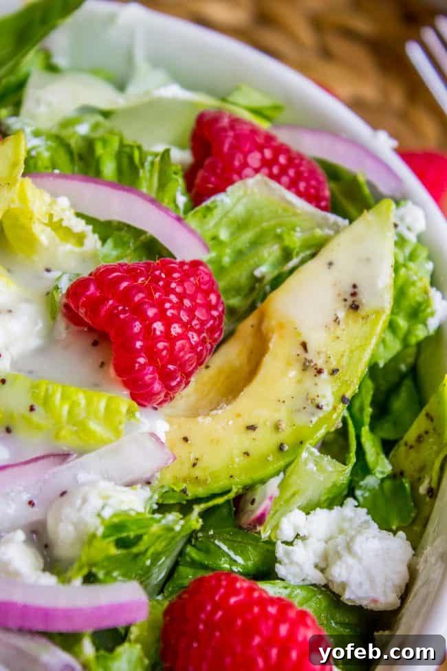 Vibrant Raspberry Avocado Salad with Poppyseed Vinaigrette 3 A close-up of an avocado salad with fresh avocado slices, raspberries, red onion, romaine lettuce, crumbled feta cheese, and a sprinkle of black pepper.