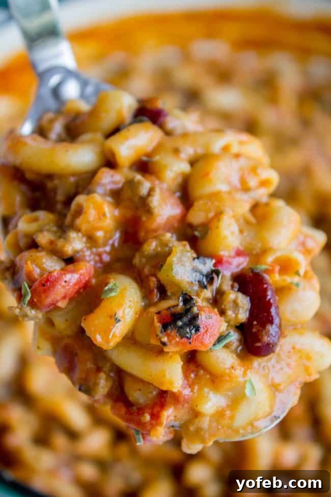 Serving Homemade One-Pot Chili Mac Hearty Chili Mac and Cheese being served from a large pot with a metal spoon, showcasing its rich texture and cheesy goodness.