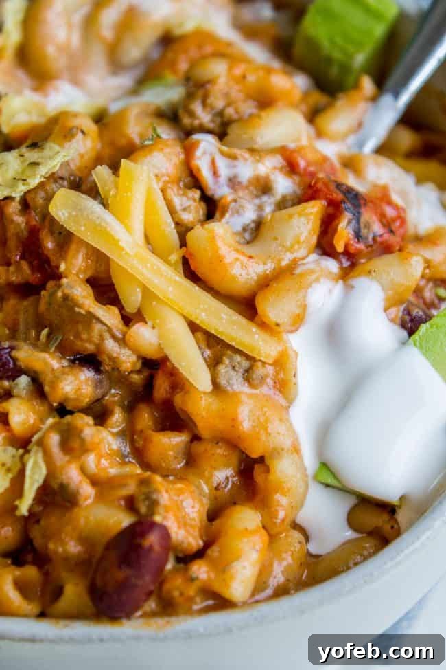 Delicious Chili Mac with Avocado and Sour Cream A vibrant bowl of Chili Mac and Cheese, generously topped with shredded cheddar, fresh avocado slices, and a dollop of sour cream.