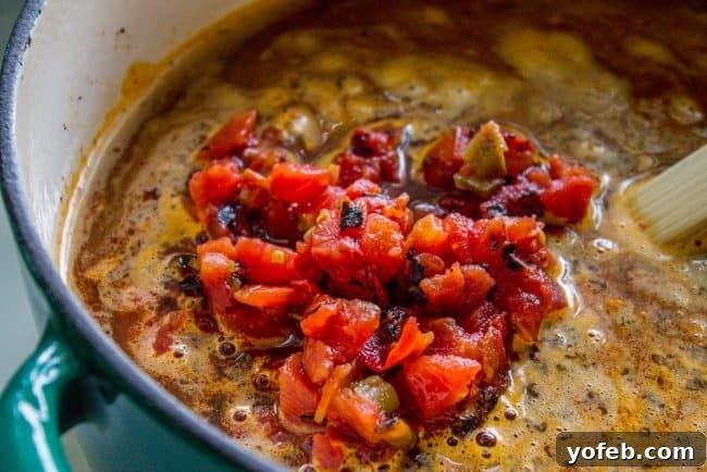 Adding Fire Roasted Rotel to Chili Mac Stirring fire-roasted Rotel (diced tomatoes and green chilis) into a pan of seasoned ground beef and onions, creating a rich chili base.