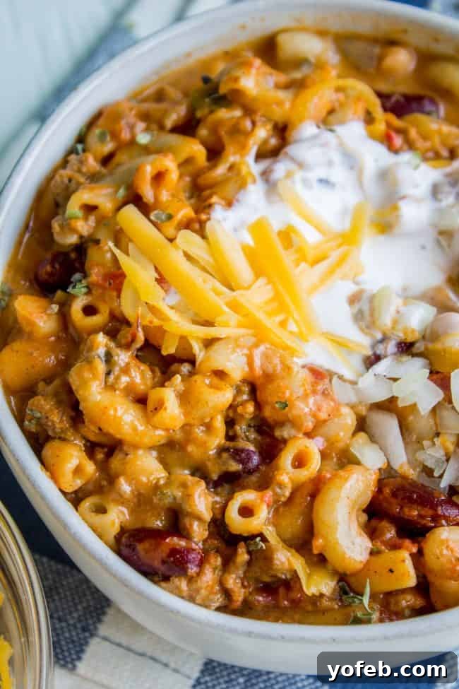 Chili Mac with Sour Cream and Shredded Cheddar A tantalizing bowl of Chili Mac and Cheese, generously topped with a dollop of sour cream and a sprinkle of shredded cheddar cheese, ready to be enjoyed.