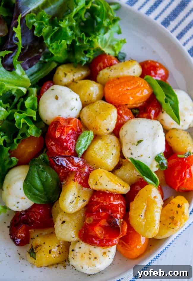 Close-up of crispy roasted gnocchi alongside sweet cherry tomatoes and melted fresh mozzarella, infused with olive oil and garlic.