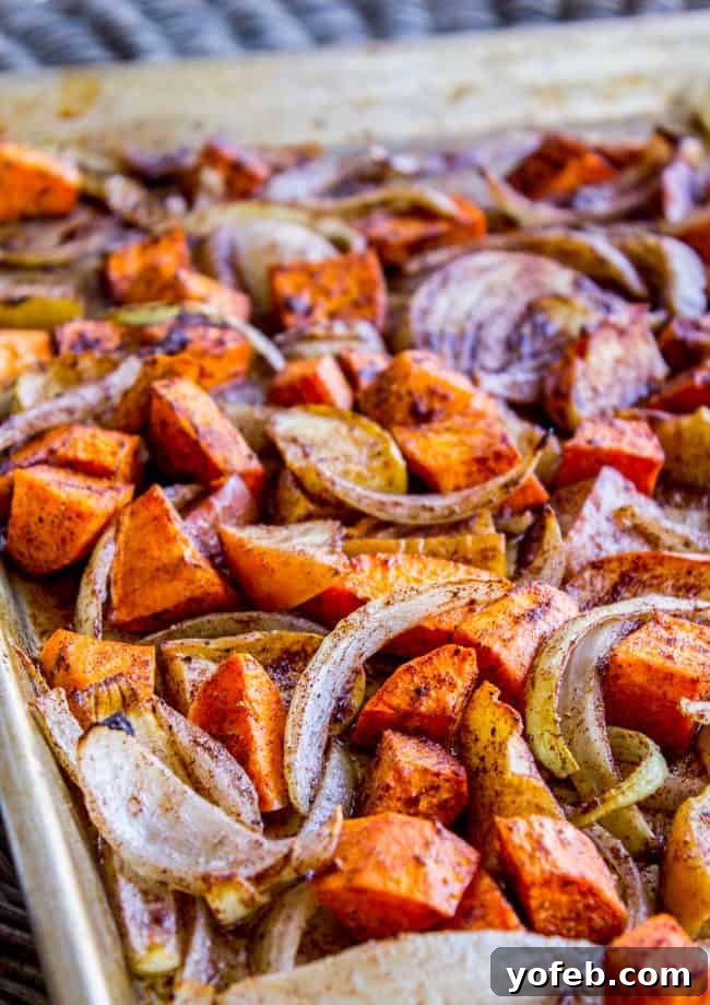 Glazed Pork Chops with Apples from The Food Charlatan. These Pork Chops with Apples are such an easy weeknight dinner! They are done in just a few minutes, and finished off in a delicious apple cider glaze. The cinnamon-spiced roasted apples and sweet potatoes will have your house smelling like autumn in no time. #apple #roasted #fall #cinnamon #applecider #onion #dinner #easy #weeknight #easy #fried #recipe #boneless #sauce #healthy #glazed A sheet pan filled with cinnamon-spiced roasted apples, sweet potatoes, and onions, ready to be served.