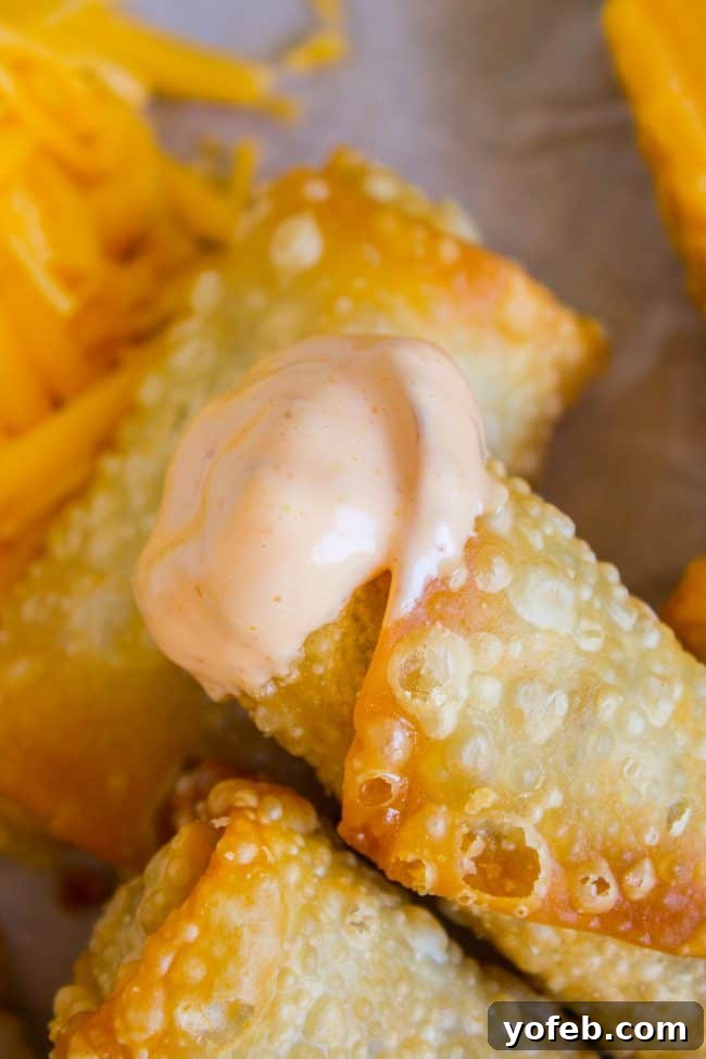 Cheeseburger Egg Rolls from The Food Charlatan. These have got to be one of the best mashups of all time! I mean, cheesy hamburger filling that's deep fried in wrappers?? How can we go wrong here? Dip it in a delicious fry sauce and you will be in cheeseburger heaven in no time! #cheeseburger #burger #hamburger #cheesy #cheese #fried #deepfried #easy #recipe #beef #homemade #howtomake #frysauce #appetizer #dip A close-up of a cheeseburger egg roll, with one end dipped into a rich, creamy fry sauce.