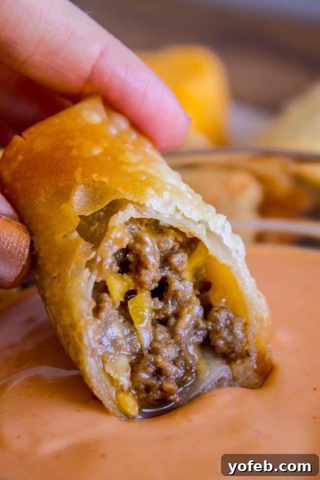 Cheeseburger Egg Rolls from The Food Charlatan. These have got to be one of the best mashups of all time! I mean, cheesy hamburger filling that's deep fried in wrappers?? How can we go wrong here? Dip it in a delicious fry sauce and you will be in cheeseburger heaven in no time! #cheeseburger #burger #hamburger #cheesy #cheese #fried #deepfried #easy #recipe #beef #homemade #howtomake #frysauce #appetizer #dip A cheeseburger egg roll being dipped into a rich, creamy fry sauce, showcasing its crispy texture.