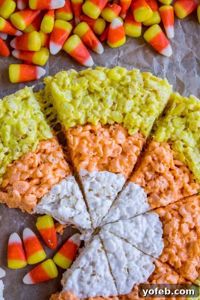 Delicious Candy Corn Rice Krispie Treats Ready to Serve Three triangular Candy Corn Rice Krispie Treats stacked on a white platter, with extra candy corn scattered around.