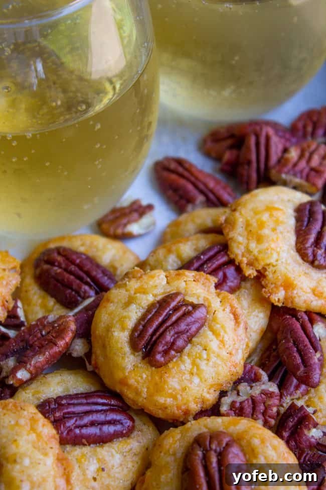 Holiday Southern Pecan Cheese Wafers 6 A hand reaching for a Southern Pecan Cheese Wafer from a small bowl, set against a festive background.