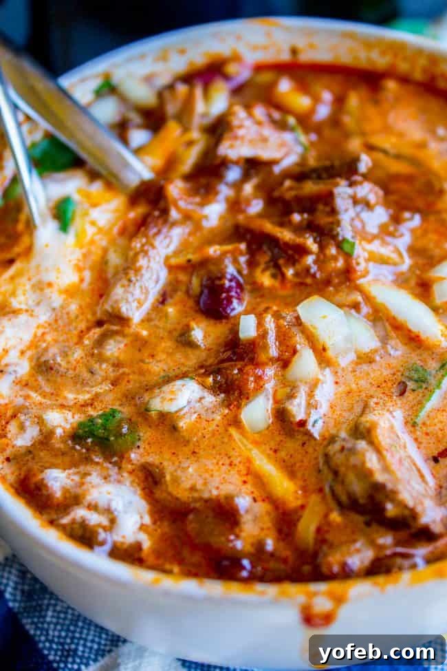 Chili with fresh garnishes - A feast for the eyes and palate. A vibrant bowl of chili with two spoons, garnished generously with fresh cilantro, a dollop of sour cream, and diced red onions, ready for sharing.