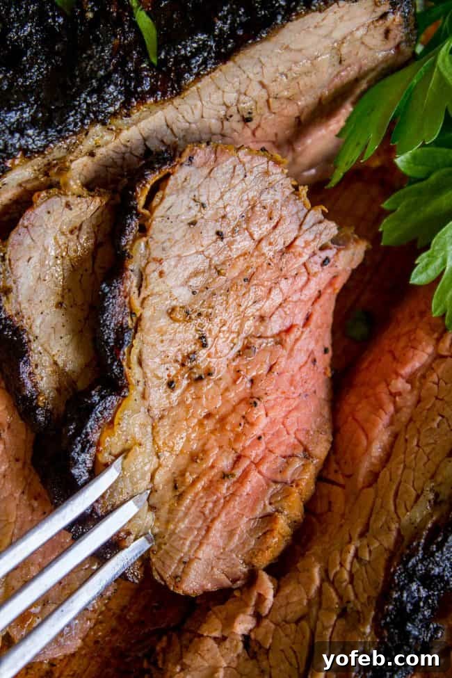 How to Cook Tri Tip (Grilled or Oven-Roasted) from The Food Charlatan. If you've never had tri tip, you haven't lived! I will show you how to cook tri tip on the grill or in the oven. It's SO easy and the flavor is unbeatable! We always had tri tip for Christmas dinner growing up; it's an impressive holiday dinner! A garlic marinade rub and tri tip roast recipe for a Christmas meal or summer bbq? Yes, please! All the tender, juicy, beefy goodness of steak but at a much more affordable price. Close-up of a perfectly cooked medium-rare tri-tip slice, with a fork gently piercing its tender surface.