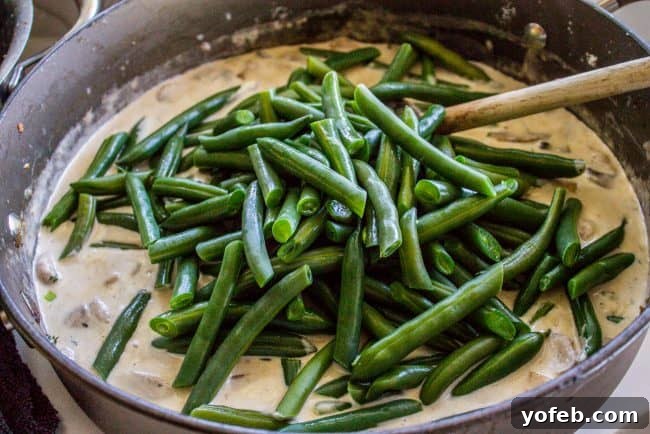 Mixing Green Beans into Creamy Sauce for Casserole Adding blanched green beans to the creamy mushroom sauce in a large skillet.