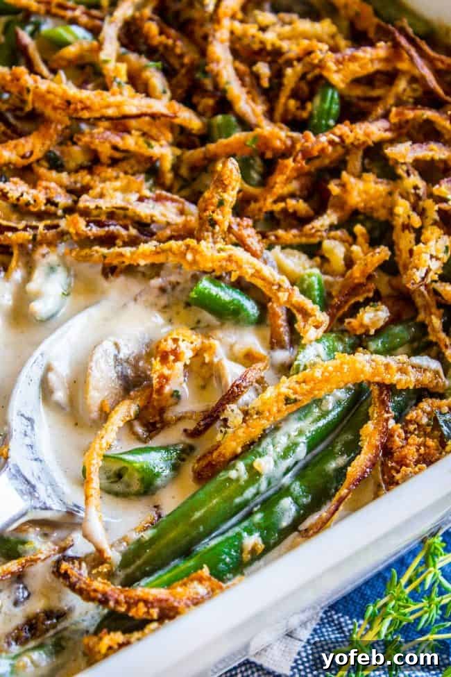 Handcrafted Fresh Green Bean Casserole 3 Close-up of green bean casserole with fresh green beans, topped with crispy fried onions and creamy sauce, as a serving spoon scoops out a portion from the baking dish.
