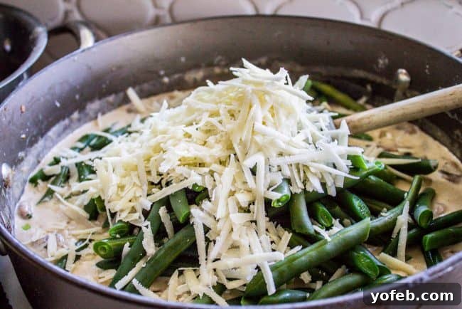Key Step: Adding Parmesan to Green Bean Casserole Adding shredded Parmesan cheese and blanched green beans to the creamy mushroom sauce in a skillet.