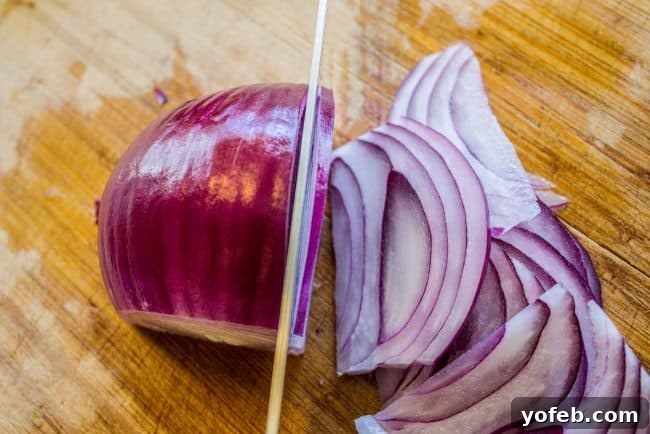 Prep Tip: How to Slice Onions for Crispy Topping Thinly slicing red onions on a wooden cutting board for homemade fried onions.