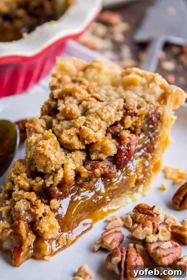 Pecan Pie Recipe with Buttery Streusel Topping from The Food Charlatan. This is not your average Pecan Pie recipe! First we brown the butter, then we adds toffee bits (which melt into a glorious caramel filling), and THEN we top it off with a supremely buttery streusel that I promise is not too sweet, but instead adds the perfect crunch. #easy #recipe #brownsugar #pecan #pie #crumble #streusel #topping #crust #homemade #best #crust #filling #caramel #toffee #brownbutter #recipe #thanksgiving a slice of streusel topped pecan pie on a white plate, showcasing a golden crust, gooey filling, and crunchy pecan-streusel topping.