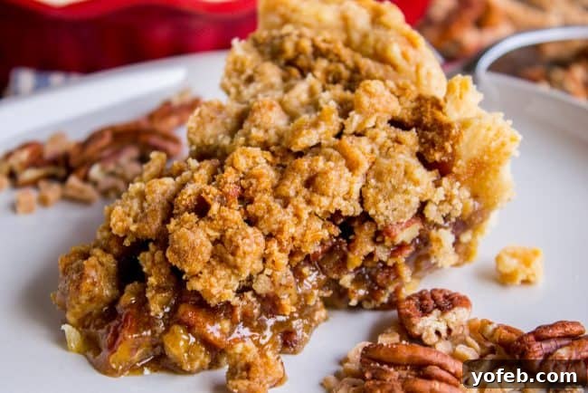 Pecan Pie Recipe with Buttery Streusel Topping from The Food Charlatan. This is not your average Pecan Pie recipe! First we brown the butter, then we adds toffee bits (which melt into a glorious caramel filling), and THEN we top it off with a supremely buttery streusel that I promise is not too sweet, but instead adds the perfect crunch. #easy #recipe #brownsugar #pecan #pie #crumble #streusel #topping #crust #homemade #best #crust #filling #caramel #toffee #brownbutter #recipe #thanksgiving A single slice of streusel-topped pecan pie on a white plate, showcasing its inviting texture and golden-brown hue.