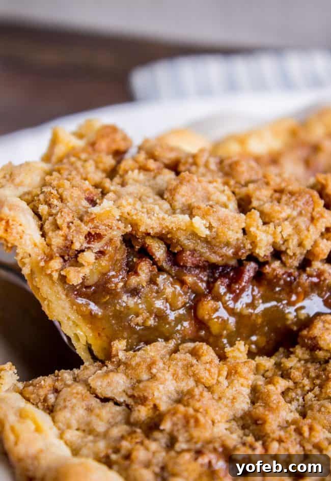 Pecan Pie Recipe with Buttery Streusel Topping from The Food Charlatan. This is not your average Pecan Pie recipe! First we brown the butter, then we adds toffee bits (which melt into a glorious caramel filling), and THEN we top it off with a supremely buttery streusel that I promise is not too sweet, but instead adds the perfect crunch. #easy #recipe #brownsugar #pecan #pie #crumble #streusel #topping #crust #homemade #best #crust #filling #caramel #toffee #brownbutter #recipe #thanksgiving A slice of gooey toffee pecan pie with streusel topping being carefully lifted from the whole pie, showing its rich texture and perfect portion.