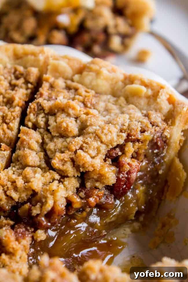 Pecan Pie Recipe with Buttery Streusel Topping from The Food Charlatan. This is not your average Pecan Pie recipe! First we brown the butter, then we adds toffee bits (which melt into a glorious caramel filling), and THEN we top it off with a supremely buttery streusel that I promise is not too sweet, but instead adds the perfect crunch. #easy #recipe #brownsugar #pecan #pie #crumble #streusel #topping #crust #homemade #best #crust #filling #caramel #toffee #brownbutter #recipe #thanksgiving gooey pecan pie with streusel topping, showing the rich, amber filling and crunchy streusel texture.
