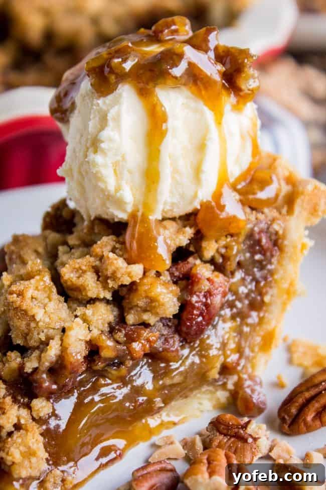 Pecan Pie Recipe with Buttery Streusel Topping from The Food Charlatan. This is not your average Pecan Pie recipe! First we brown the butter, then we adds toffee bits (which melt into a glorious caramel filling), and THEN we top it off with a supremely buttery streusel that I promise is not too sweet, but instead adds the perfect crunch. #easy #recipe #brownsugar #pecan #pie #crumble #streusel #topping #crust #homemade #best #crust #filling #caramel #toffee #brownbutter #recipe #thanksgiving a slice of streusel topped pecan pie with a generous scoop of vanilla ice cream and a drizzle of caramel sauce, emphasizing its luxuriousness.
