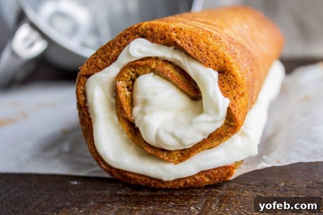 Close-up of a pumpkin roll with thick cream cheese frosting, being carefully rolled again without the parchment paper.