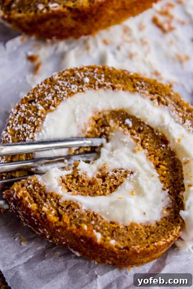 A close-up of a slice of pumpkin roll cake with cream cheese filling, partly eaten with a fork, resting on parchment paper. The cake appears moist and lightly dusted with powdered sugar.