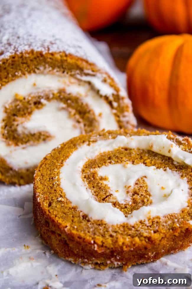 A full pumpkin roll with a single slice cut and resting on the side, revealing the creamy filling and cake texture.