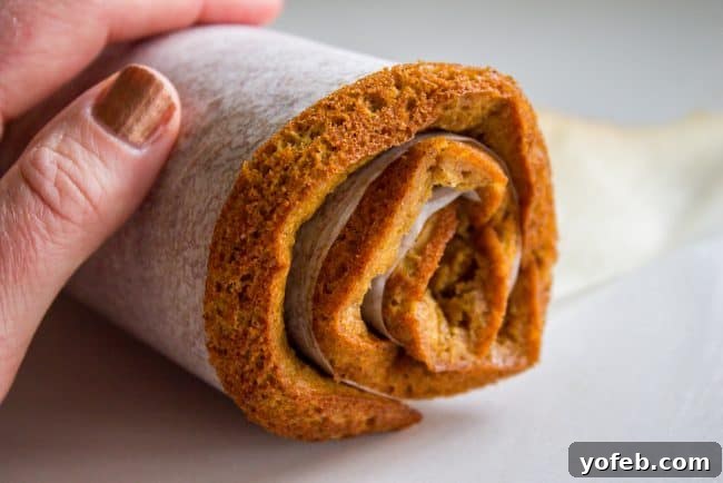 The baked pumpkin cake being rolled carefully with parchment paper and powdered sugar immediately after coming out of the oven.