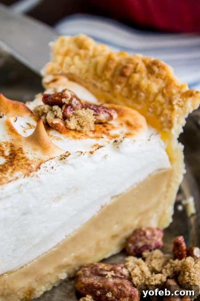 A close-up of a slice of butterscotch meringue pie on a white plate, showcasing the thick, creamy filling and towering, toasted meringue.