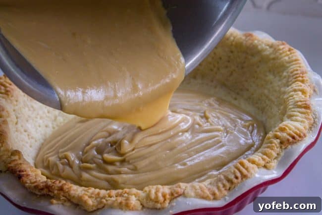 A close-up of a slice of butterscotch pie, showing the layers of golden crust, smooth pudding, and peaks of toasted meringue.