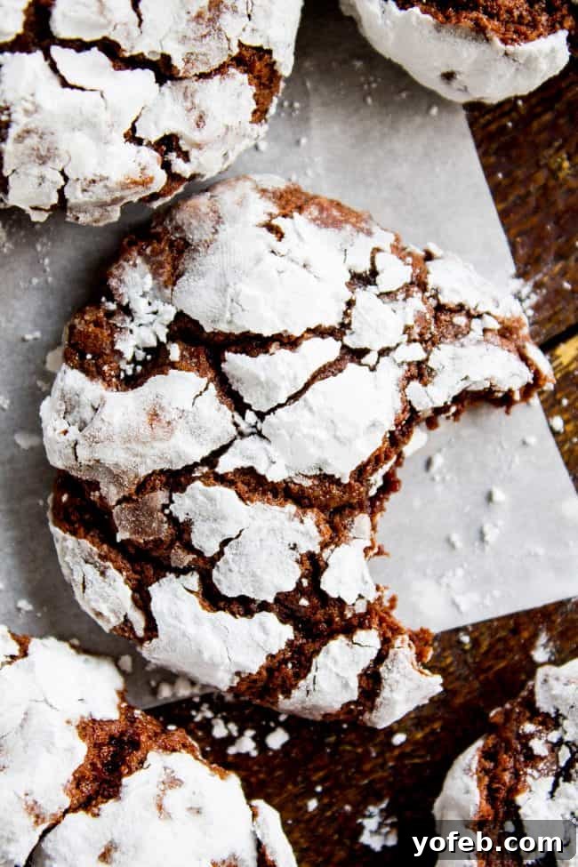 Freshly baked chocolate crinkle cookies cooling on parchment paper, with one cookie showing a perfect bite mark, revealing its rich, fudgy interior.