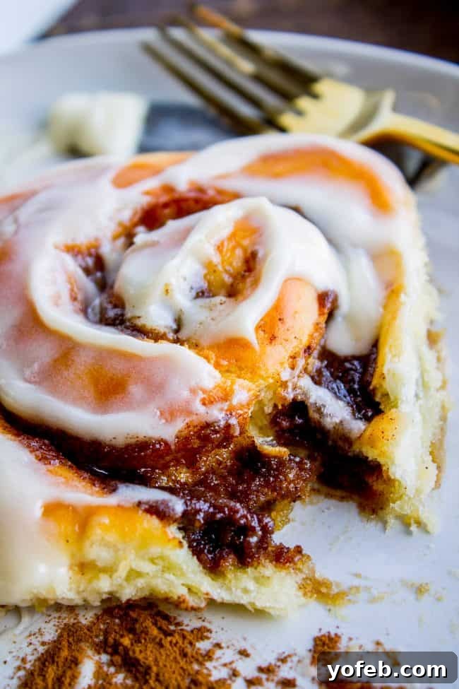 A single, fluffy iced cinnamon roll on a plate with a fork, emphasizing its tender texture and delicious frosting swirl.