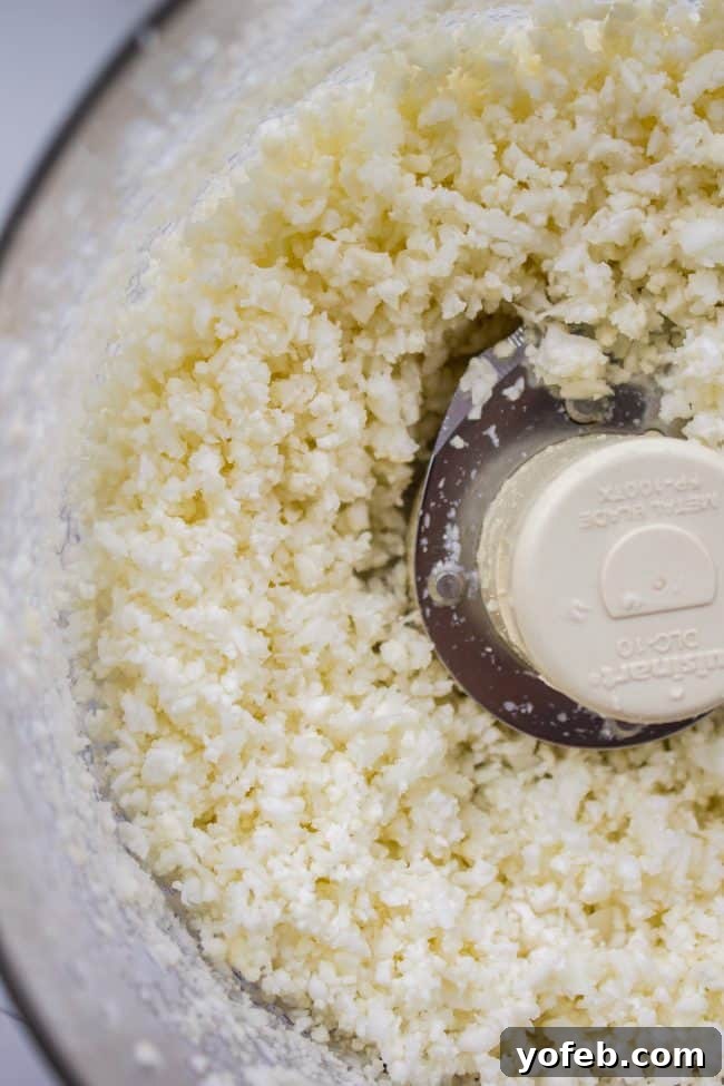 Cauliflower florets being processed into rice-like grains in a food processor.