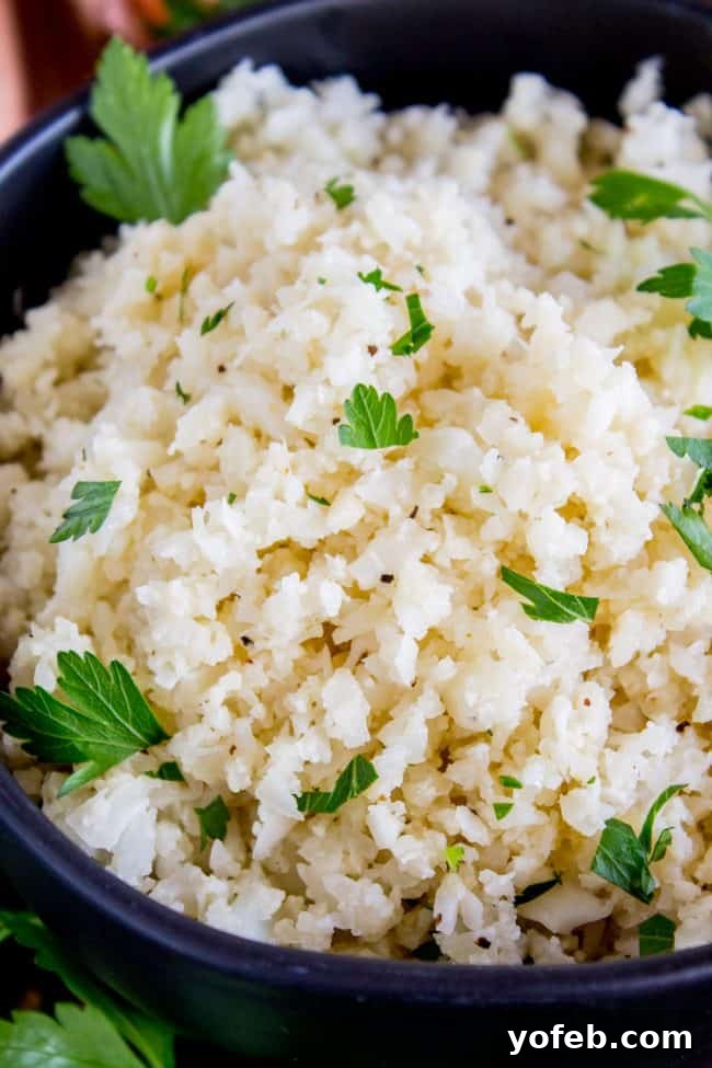 A black bowl brimming with freshly cooked cauliflower rice and topped with vibrant green cilantro.
