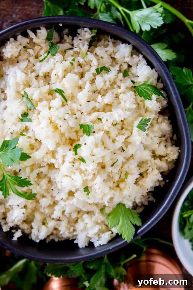 A black bowl filled with cauliflower rice and fresh cilantro, placed on a wooden surface beside salt and pepper shakers.