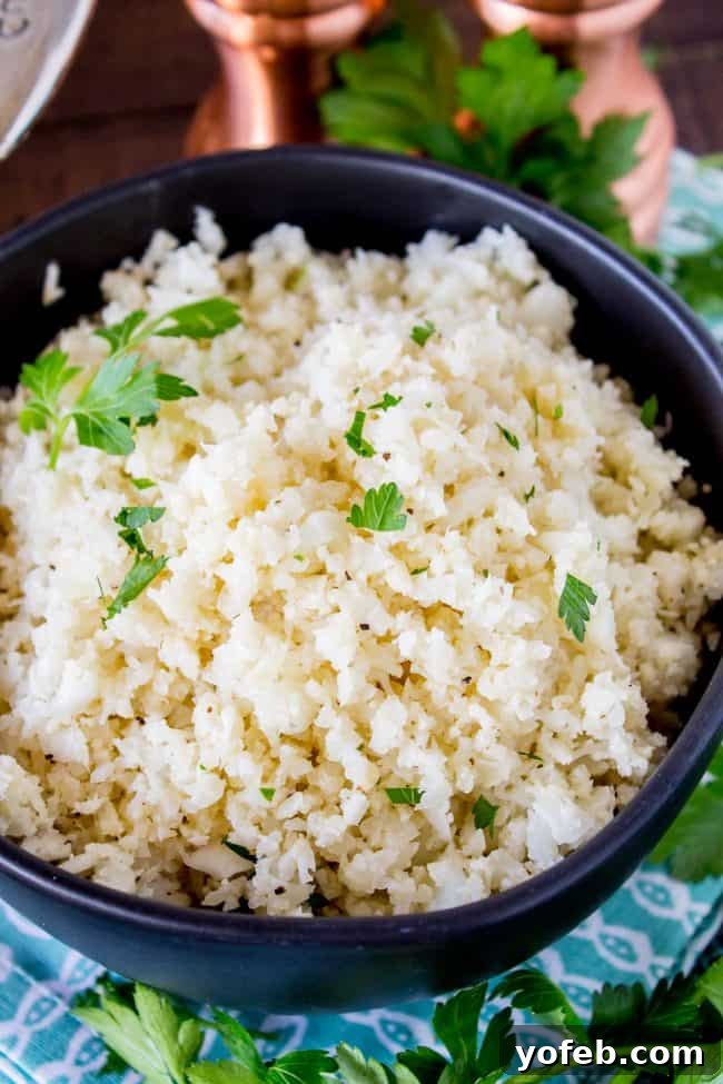 Close-up of fluffy cauliflower rice garnished with green herbs in a black ceramic bowl, set against a rustic wooden background.